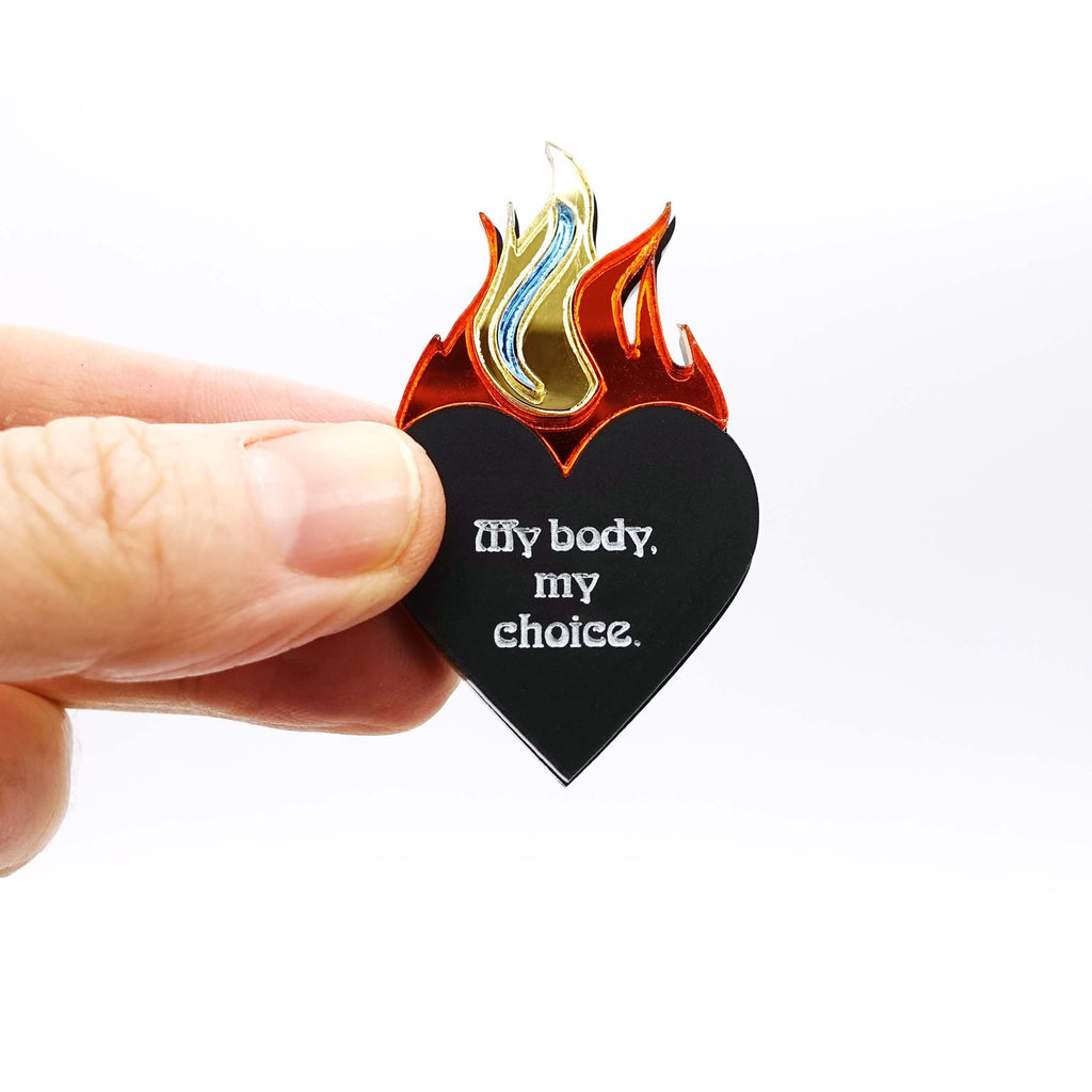 My body my choice flaming heart brooch designed by Sarah Day for Wear and Resist shown being held for size. 