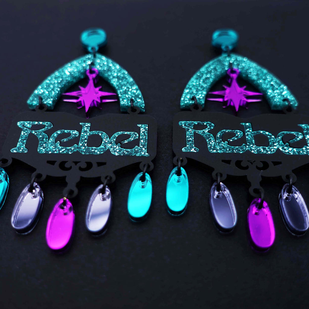 Pair of rebel rebel statement earrings on black background in mirror purple and teal glitter