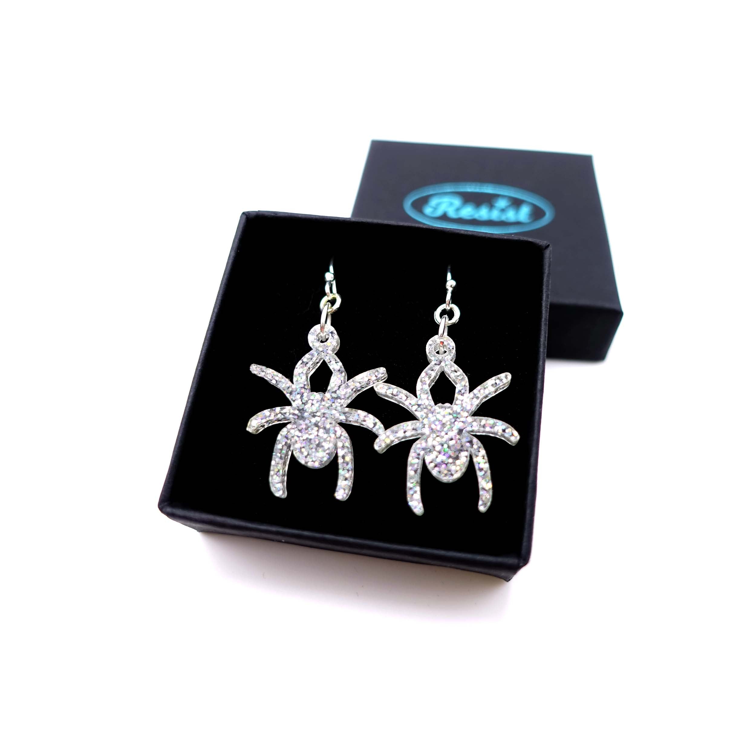 Lady Hale commemorative spider earrings in iridescent silver glitter shown in box.