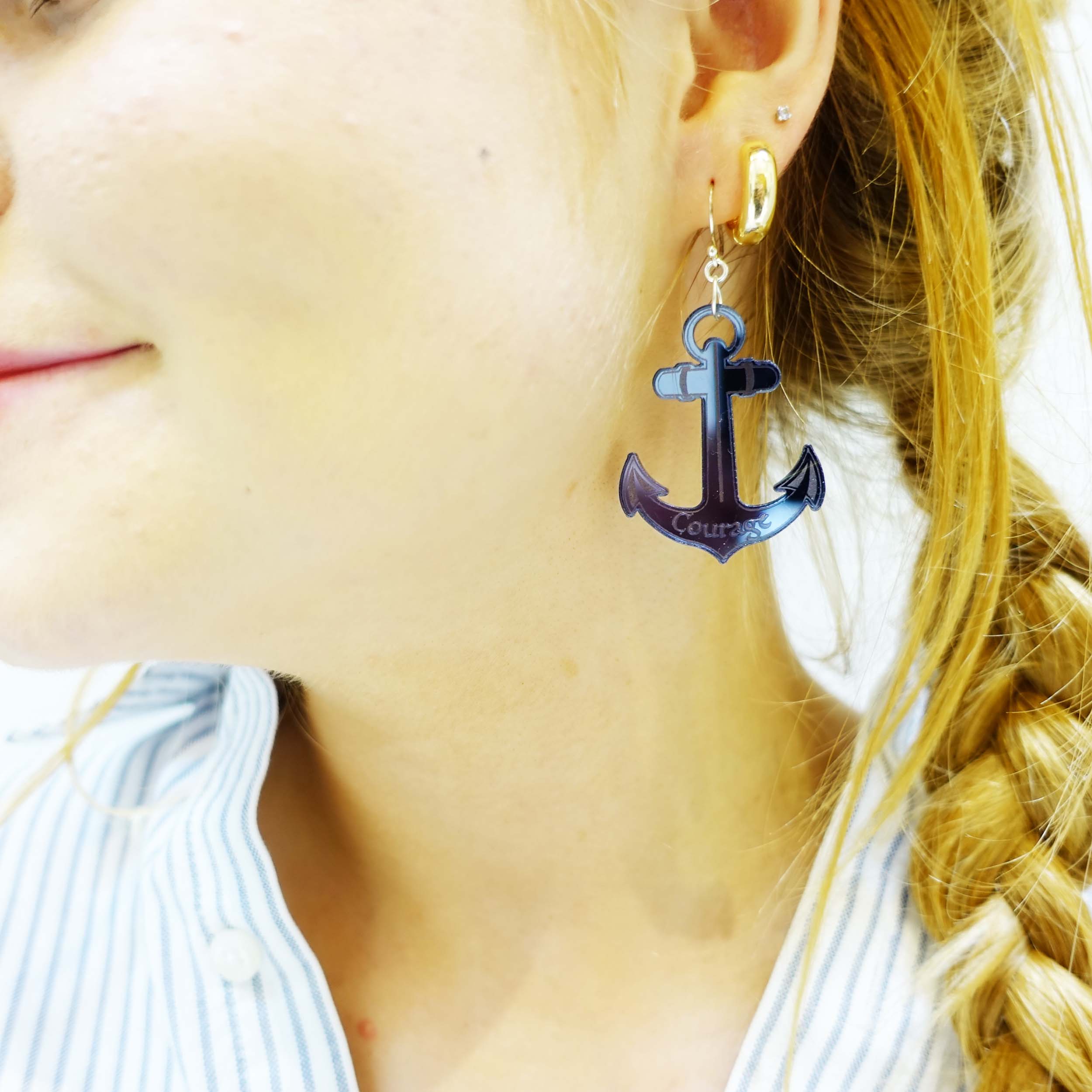 Model wears slate mirror Anchor earrings, showing one etched with the word courage, with proceeds to go to the RNLI and Women for Refugee Women