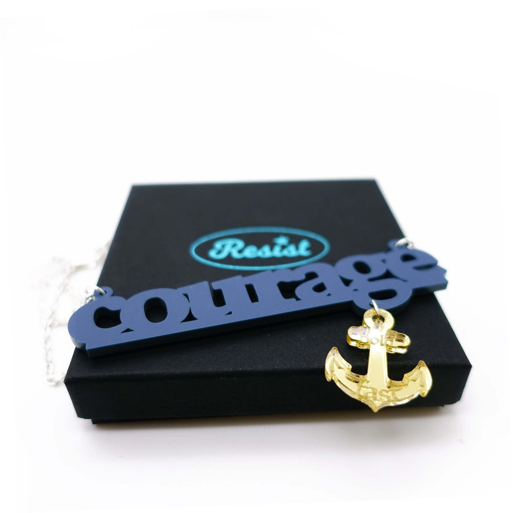 Courage necklace to benefit the RNLI and Women for Refugee Women in slate with a gold mirror anchor etched with the words 'hold fast,' shown on gift box. 
