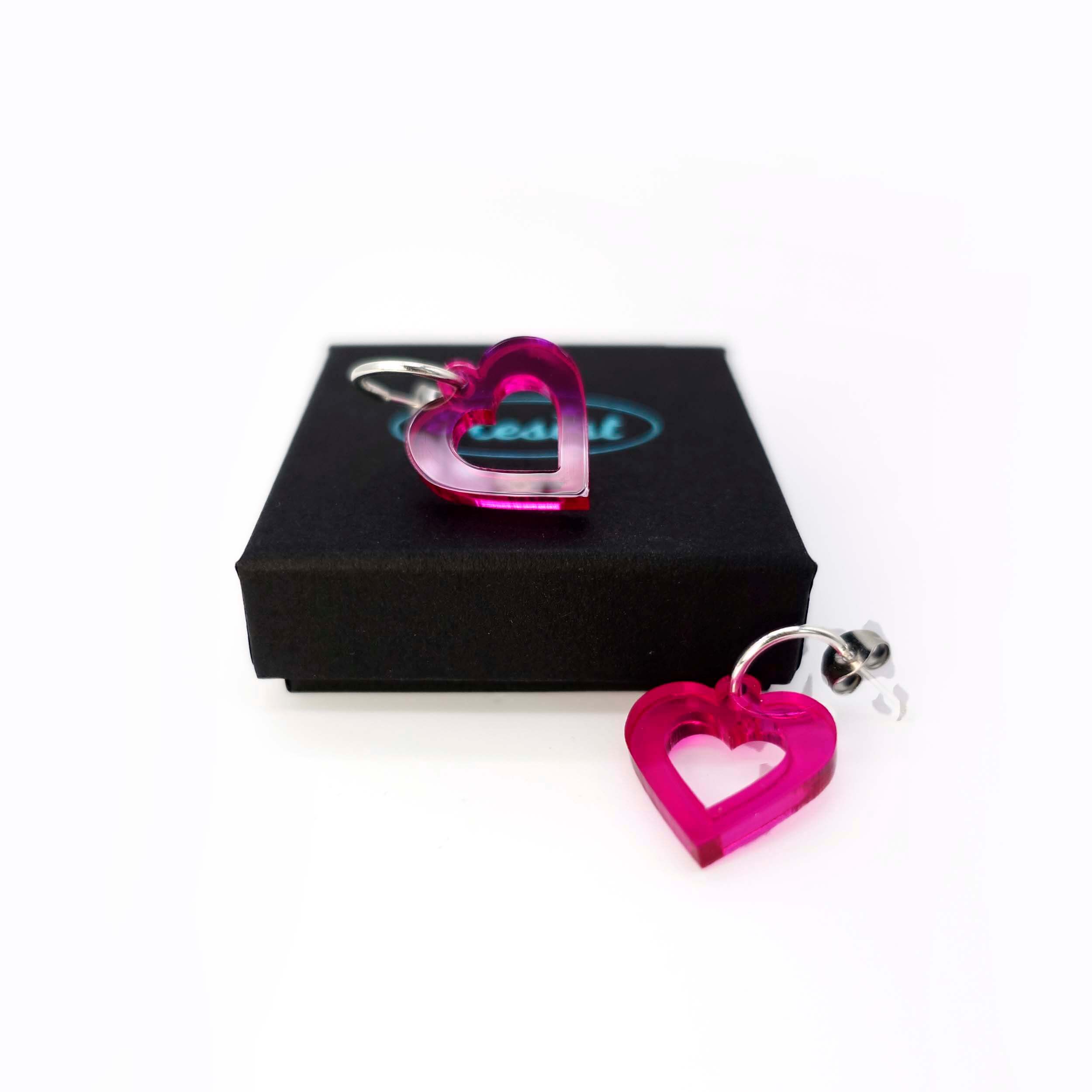 Small transparent hot pink love heart earrings shown one on a Wear and Resist gift box and one on the white background. 