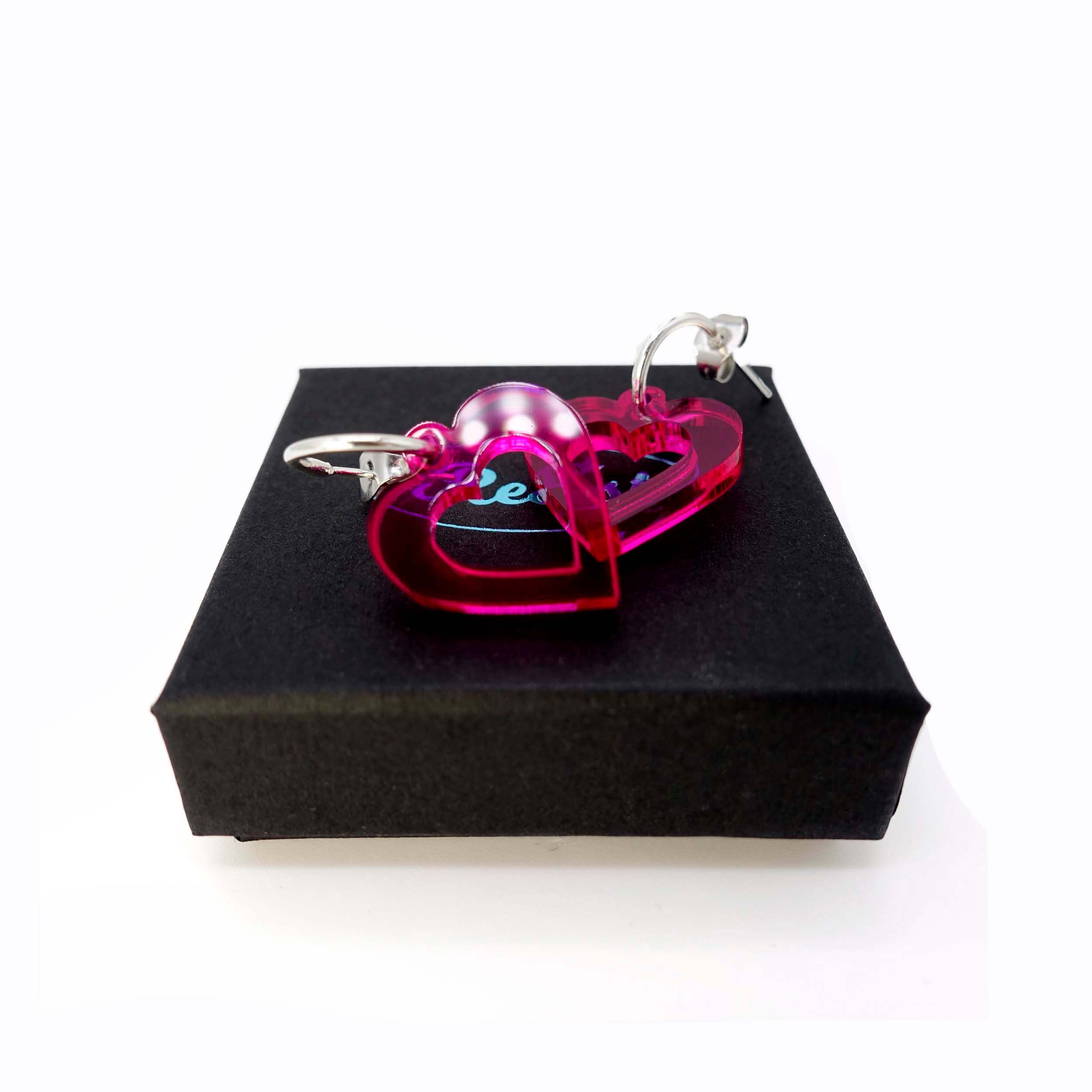 Transparent hot pink small love heart hoop earrings shown on a Wear and Resist gift box. 
