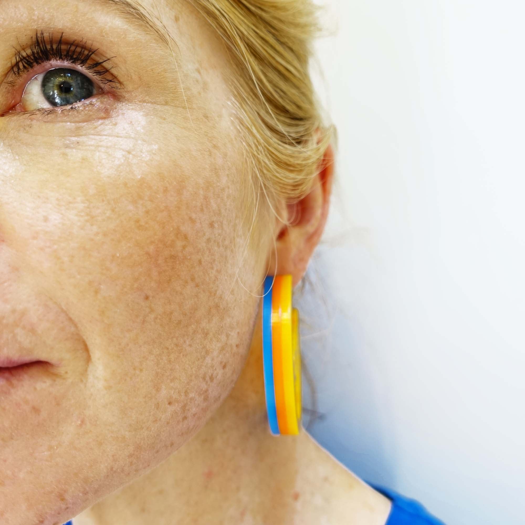 Model wears Roller Disco sunflower yellow orange and blue Suffragette trio in Parma violet, white and avocado Mary Beard Women & Power earrings, statement hoops