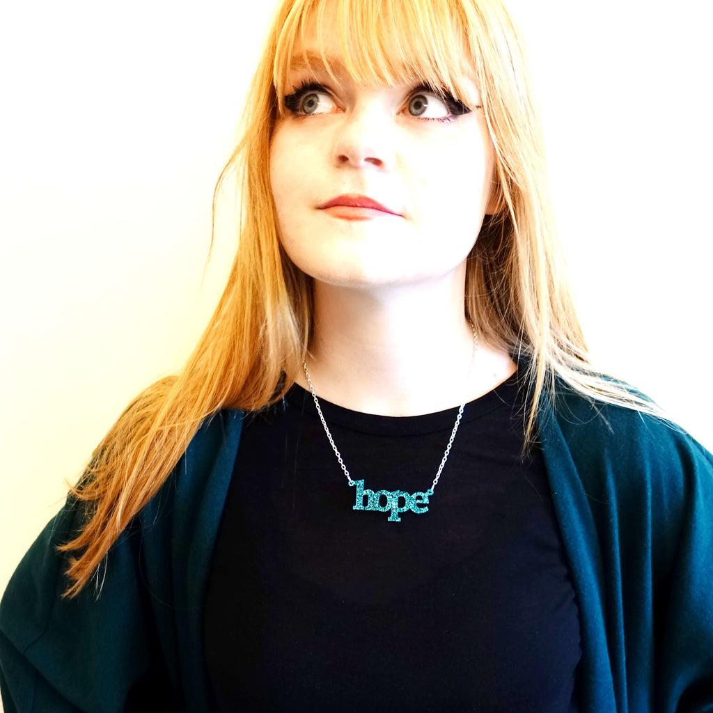 Model wears a teal glitter Hope necklace designed by Sarah Day for Wear and Resist. 